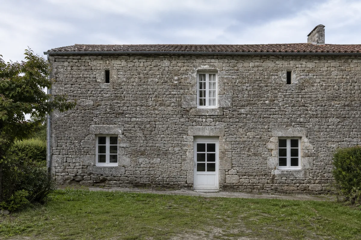 Façade en pierre de granit d&rsquo;une maison ancienne de bourg avec chaudière murale visible par la fenêtre