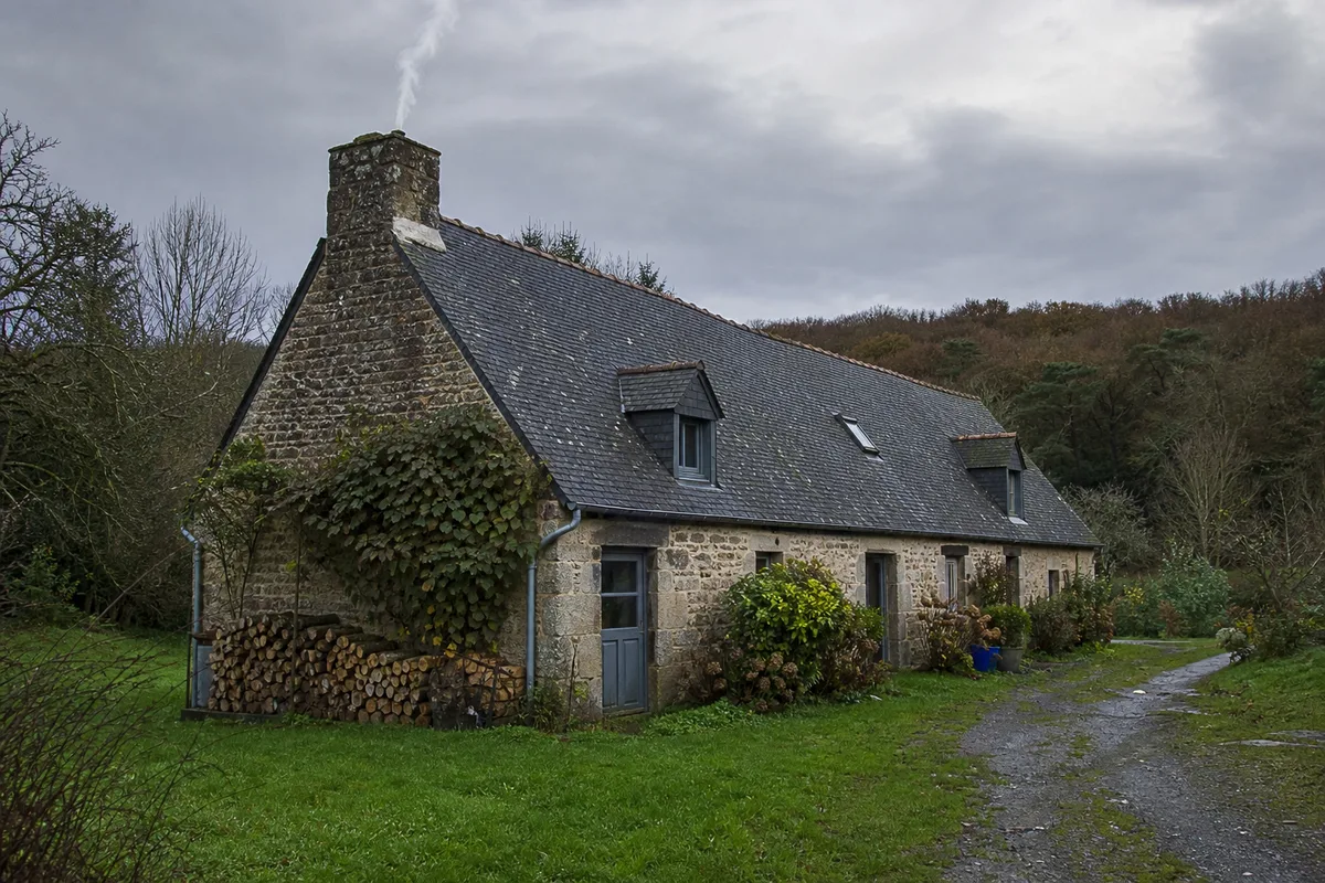 Longère bretonne en granit sous un ciel couvert, symbole du bâti à chauffer autour de Quimperlé